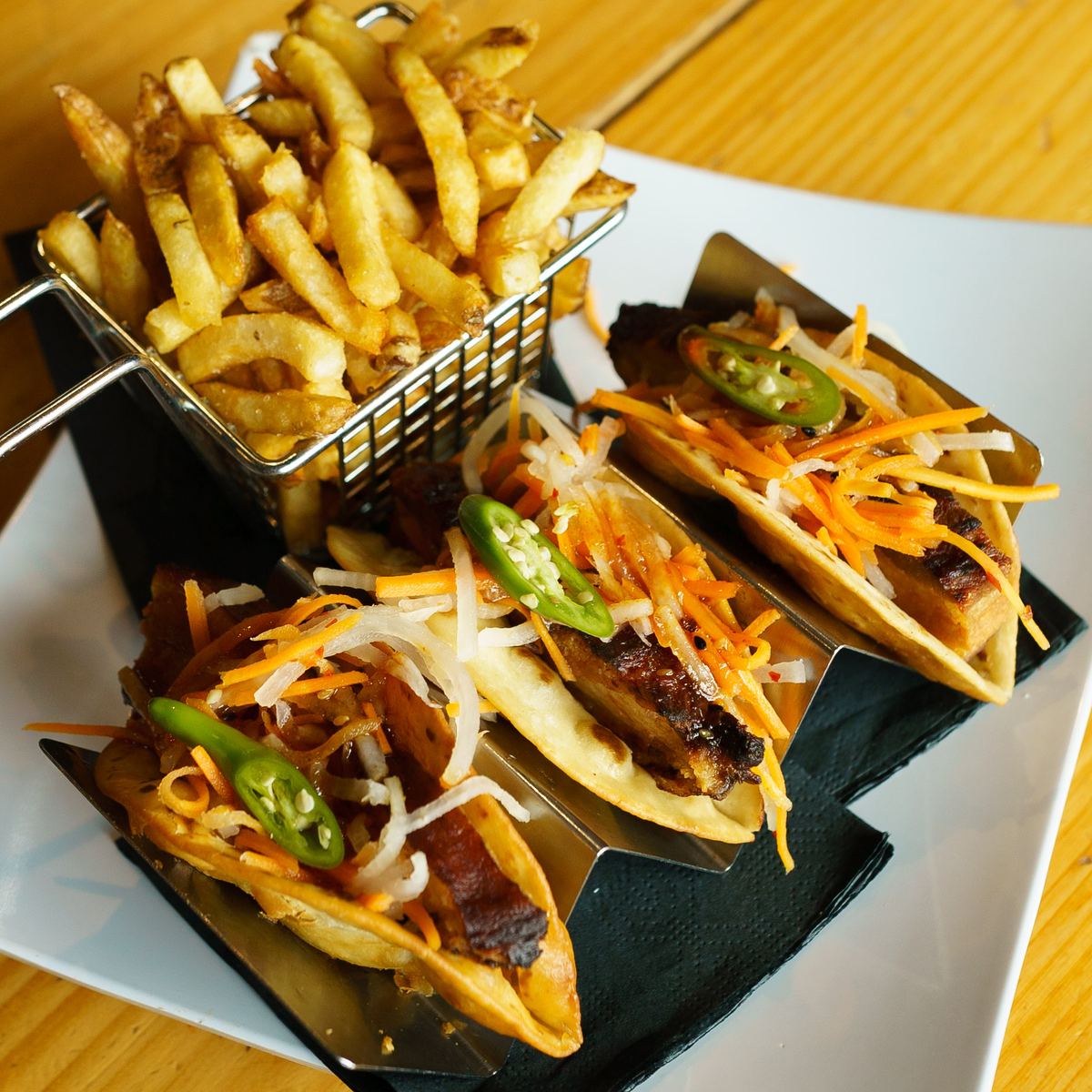 Tacos with sliced jalapeños and a basket of fries
